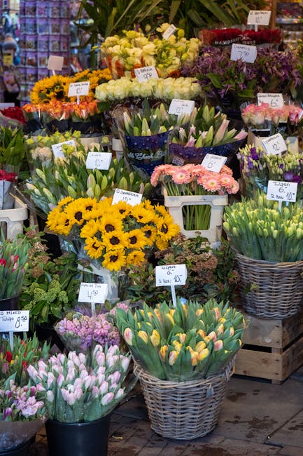 A vibrant display of fresh flowers at a florist shop, featuring sunflowers with bright yellow petals and dark centers, pink and purple tulips with smooth, elongated petals, and clusters of white and p