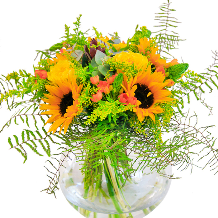 The first impression of this exquisite Stepney bouquet is one of rich exuberance, reminiscent of sunlit afternoons spent near Stepney Green. Towering sunflowers, their velvety petals reaching outward in gold and amber, form the heart of the arrangement, radiating warmth and energy. Alongside, tightly furled yellow garden roses unravel their spiral forms, offering a luxurious, classic contrast that softens the sunflowers' boldness. Deep green foliage and airy, vine-like sprigs cascade gracefully, echoing the lush gardens and hidden green spaces tucked throughout the East End. Dotted throughout are glossy hypericum berries in a lively shade of red, their round forms sparkling among the variegated greens like cheerful notes in a summer melody. The bouquet, artfully assembled in a spherical glass vase, reveals the network of strong, fresh stems and glistening water-details that highlight the care and craftsmanship typical of Flowers Stepney. Up close, subtle textures interplay: the suede surface of the sunflowers, the velveteen rose petals, and the crisp edges of eucalyptus leaves. This bouquet carries the gentle yet invigorating fragrance of fresh blooms mingled with leafy greens, making it an ideal welcome for celebratory gatherings or as a thoughtful gesture for anniversaries and milestones. Each flower and leaf tells the story of Stepney's vibrant community and the skilled hands that bring beauty to every doorstep.