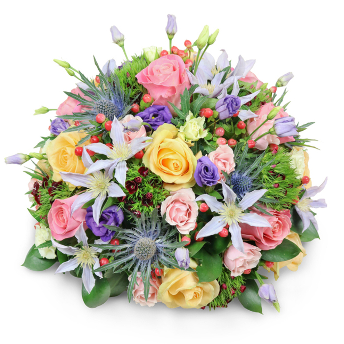 Set against a clean, white background, this meticulously arranged domed bouquet appears almost like a living sculpture, its rounded form echoing the curve of a market stall display along Stepney High Street. The flowers are packed tightly so that no stems or gaps are visible, only layers of colour and form. The primary impression is one of soft romance, led by abundant garden roses in delicate pastel shades: light pink, buttery yellow, and creamy peach. Each rose shows a different moment in its life cycle-some blossoms fully open with generous, ruffled petals forming intricate spirals, others still partially closed, giving the arrangement a natural, evolving feel. Interwoven among the roses are elegant clematis flowers, their petals long and slender, painted in white and gentle lavender to pale violet, with striking yellow or bright white centers. These star-like blooms bring a sense of airy lightness, as if a garden vine had been coaxed delicately into the hand-tied design. In contrast, blue eryngium, or sea holly, introduces a more rugged, sculptural note; its spiky, thistle-shaped heads in metallic blue-grey punctuate the softness and draw the eye, hinting at wild meadows beyond the city. Deeper purple lisianthus blooms, some in tight buds and others opening into soft, ruffled cups, add a rich undertone, while scattered clusters of shiny, bright red Hypericum berries create vivid points of colour and playful texture. Surrounding all of this is a bed of mixed greenery: broad, glossy leaves form a supportive base, finer feathery foliage threads between the flowers, and occasional hints of darker, burgundy-toned leaves add visual depth, like the shaded corners of a local park. The bouquet feels abundant yet refined, an ideal centerpiece or gift for birthdays, anniversaries, or quiet gestures of appreciation, ready to be delivered to homes and offices around Stepney with an air of polished, professional floristry.
