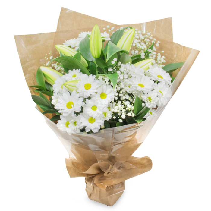 Set against a plain, bright white background, a graceful bouquet of white and green flowers appears almost to float, every stem carefully placed by a local Stepney florist with sympathy and calm in mind. The main body of the arrangement is formed by numerous white daisy chrysanthemums, their petals pristine and slightly curved, creating soft, rounded discs around luminous yellow-green centres that draw the eye again and again. These daisies nestle tightly together, giving the bouquet a full and cushioning texture. Rising between them are several elegant lily buds, their long, pointed forms closed and serene, pale green along the length with hints of creamy white at the tips, suggesting blossoms that will slowly open over the coming days, extending the life of the tribute. Light, cloud-like clusters of white gypsophila are woven gently through the display, the tiny blossoms suspended on fine stems and adding an airy, almost whispering presence. Encircling the flowers, rich green foliage with a dark, glossy surface provides structure and contrast, its sturdy leaves highlighting the delicacy of the white petals. The stems are brought together at the base and wrapped in a snug layer of rustic brown kraft paper, slightly textured and folded with care, then covered by a sheer, protective layer of clear cellophane. This double wrapping both secures the arrangement and gives it a polished, ready-to-deliver appearance, as though prepared for a thoughtful delivery to a family near Stepney City Farm or a quiet flat overlooking the Regents Canal. The overall impression is one of purity, respect, and gentle support, making the bouquet a suitable choice for expressing heartfelt sympathy or get-well wishes in and around Stepney.